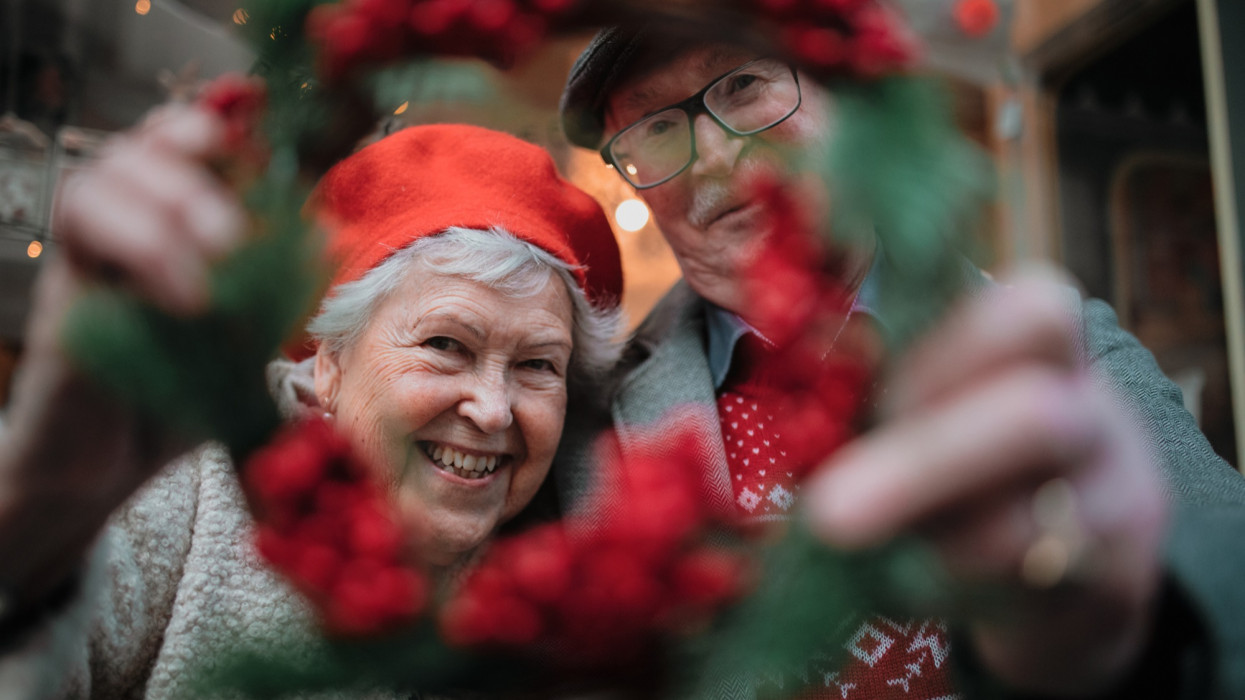 Happy senior couple at Christmas market looking trough Christmas wreath.