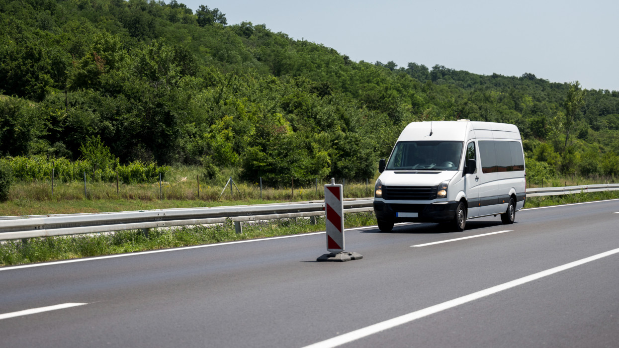 White modern delivery small shipment cargo courier van moving fast on motorway road to city urban suburb.