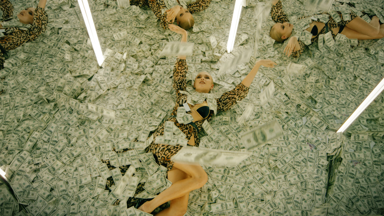 Mirror maze with a woman lying down on piles of money. Hundred dollar bill banknotes raining from above. Multiple angle view