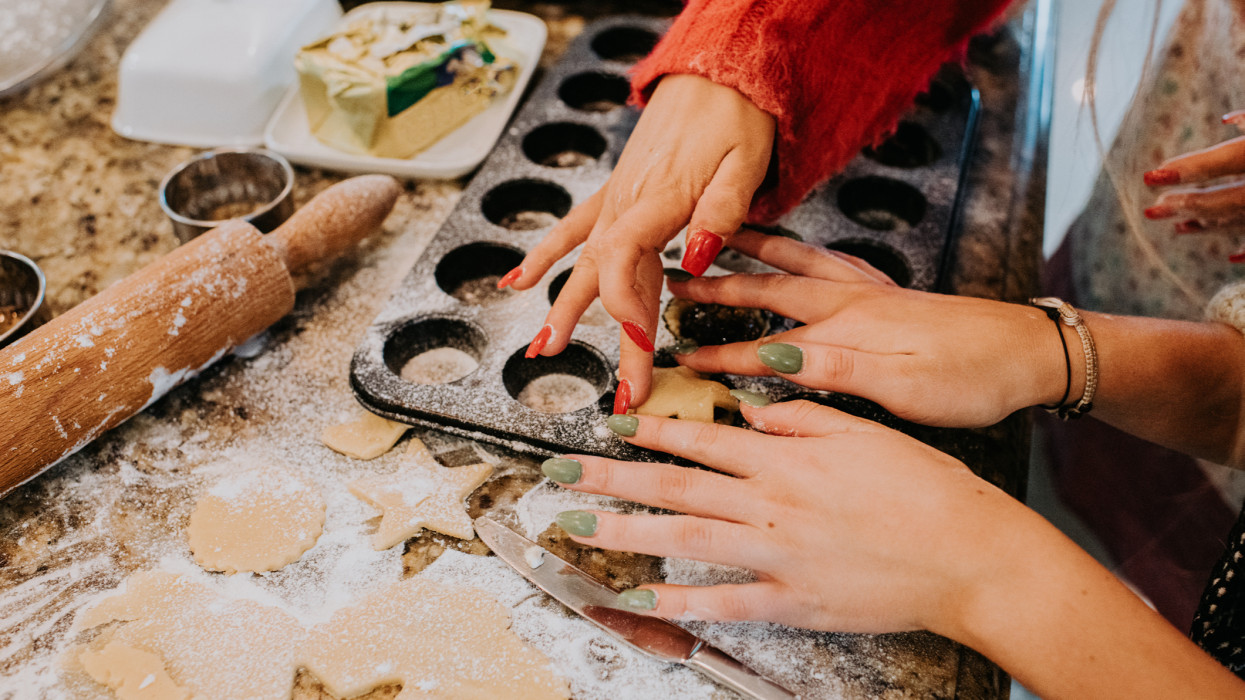 Two young woman bake mince pies. The image is a top down close-up view of their hands, with perfectly manicured nails in festive colours. Space for copy.