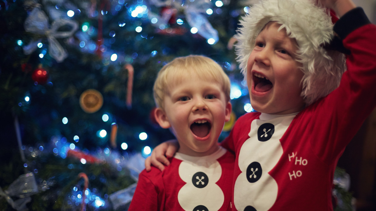 Two excited little boys singing by the Christmas tree on Christmas Eve.