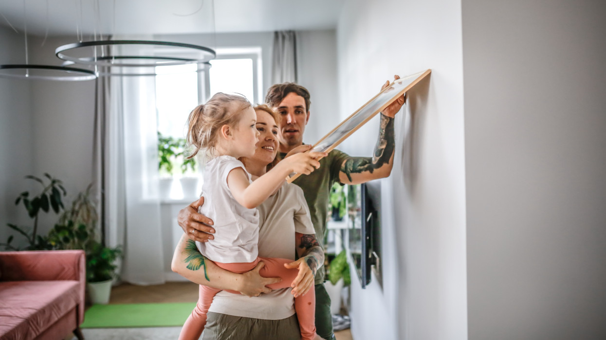 Family with one child hangs picture on wall together, moves and furnishes apartment together.