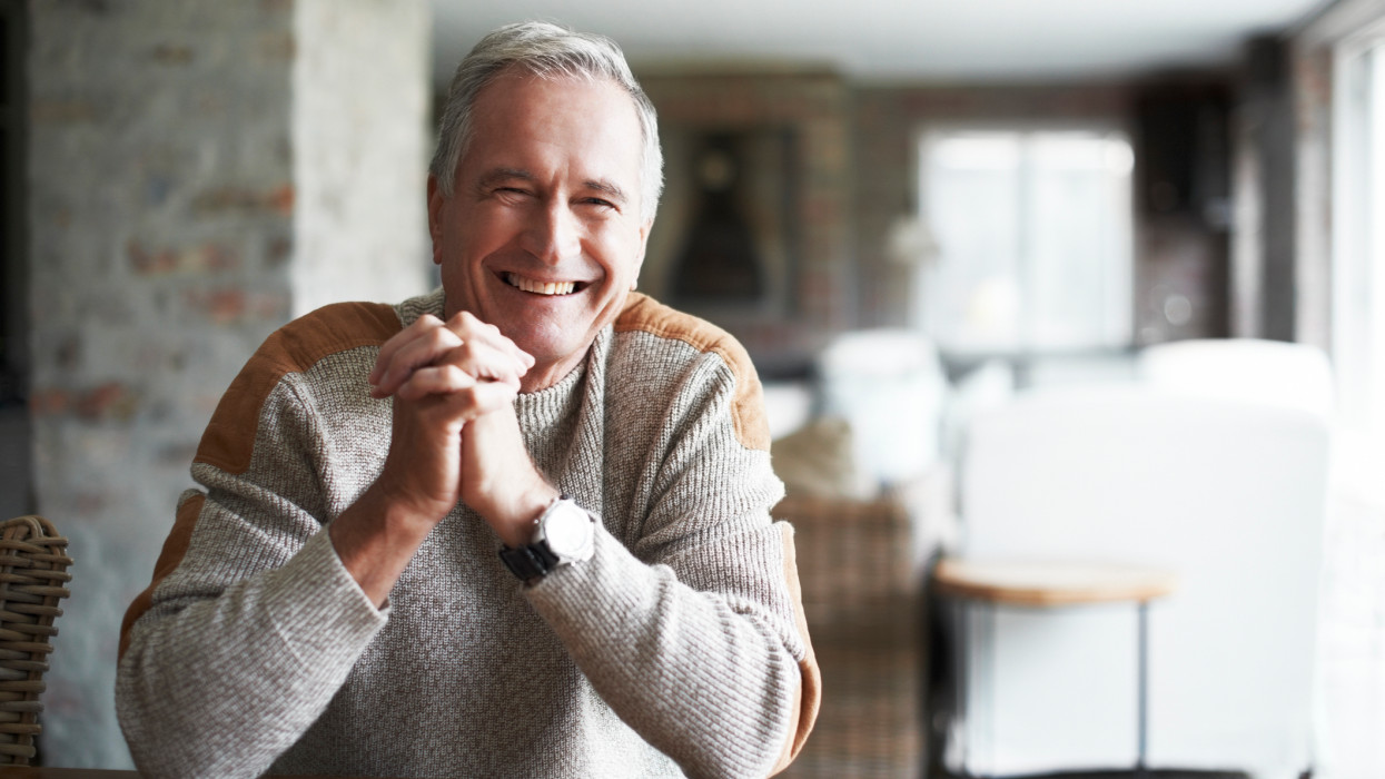 Portrait of happy senior man with hands clasped standing in house