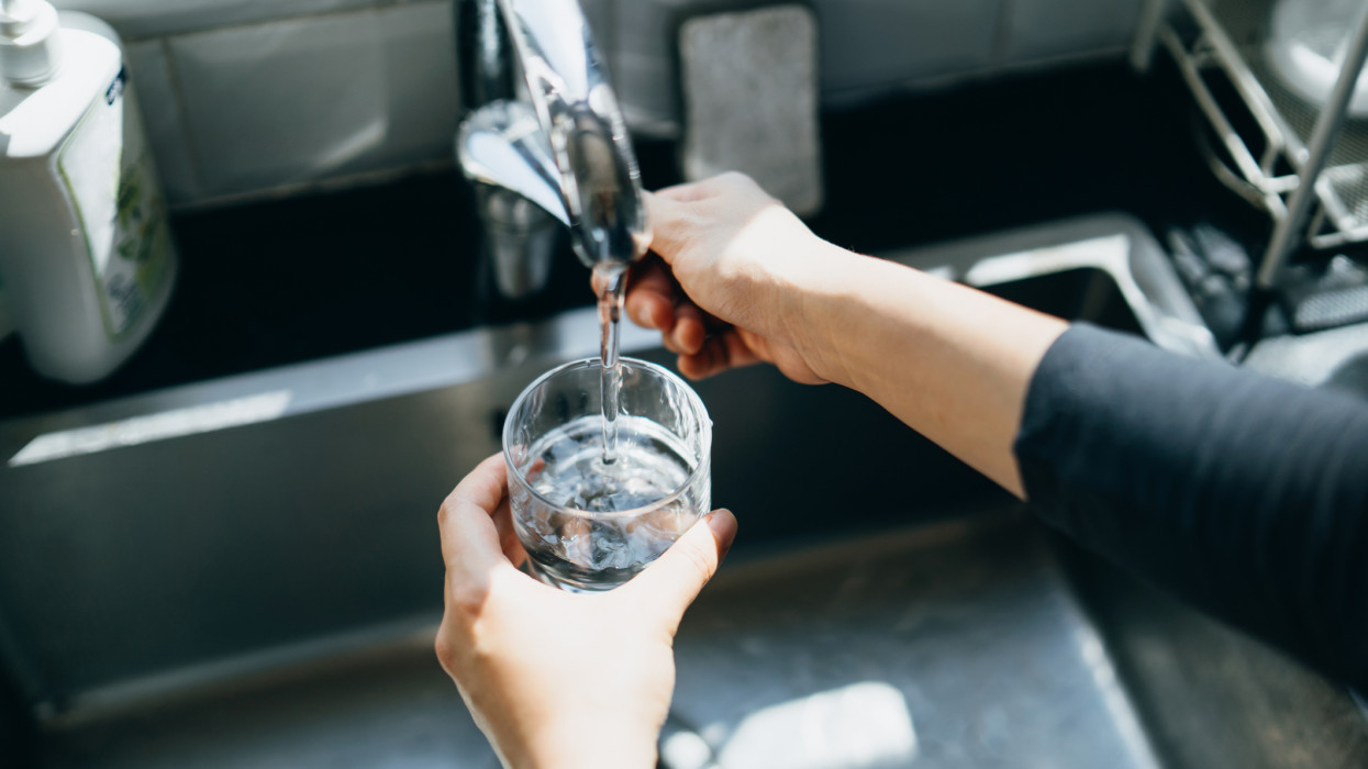 Cropped shot of womans hand filling a glass of filtered water right from the tap in the kitchen sink at home