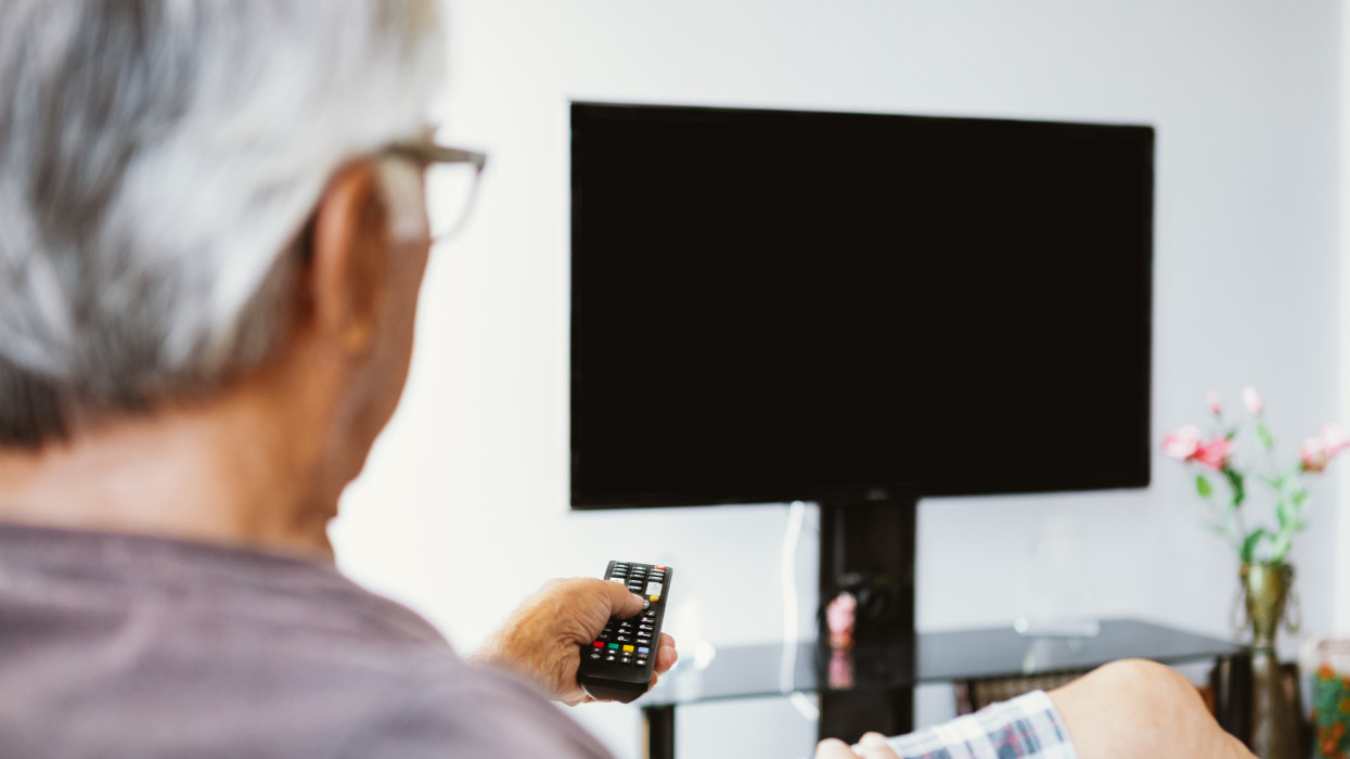 Senior man watching TV at home.  A senior man is trying to find something interesting on tv to pay attention to. Channel surfing is the practice of quickly scanning through different television channels.