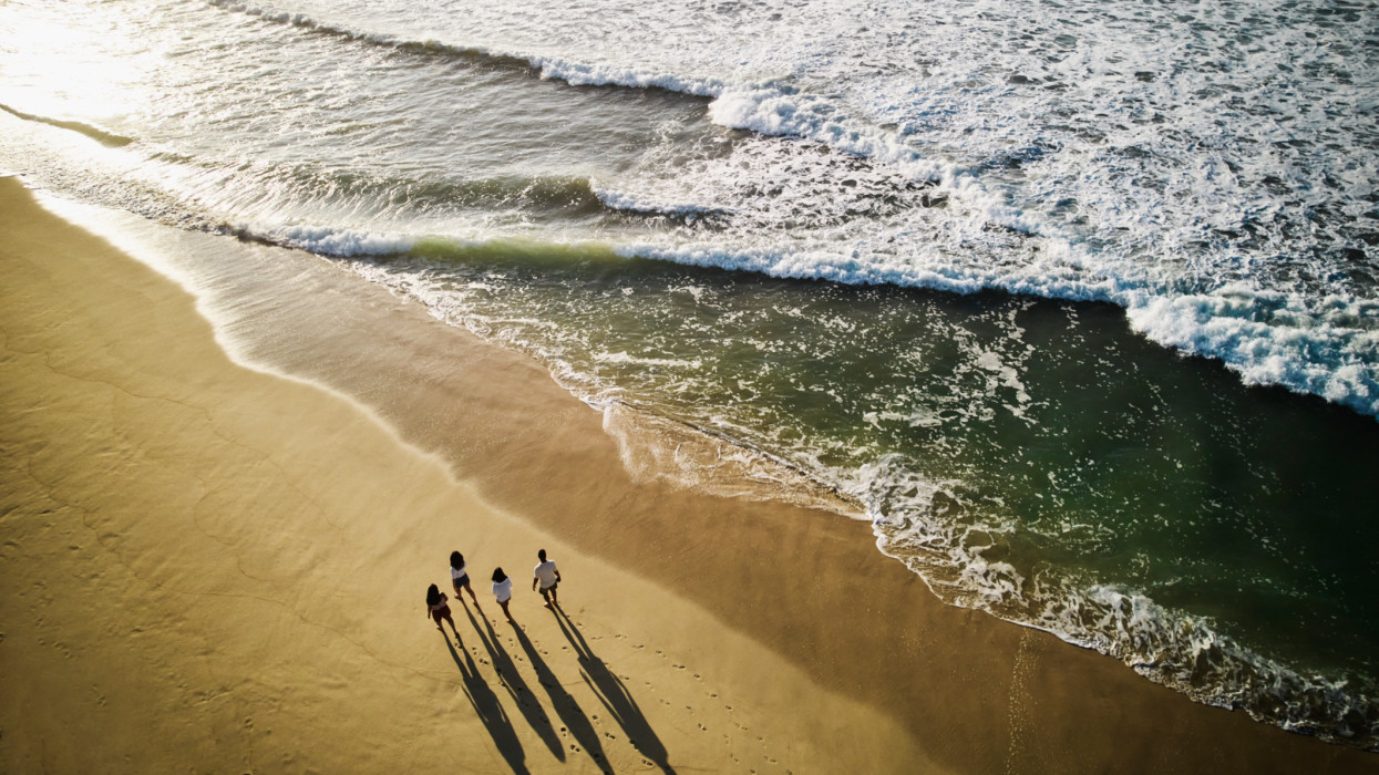 Wide aerial shot of family walking on tropical beach at sunrise while on vacation