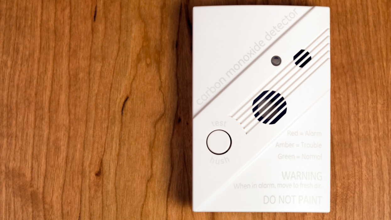 A new wall-mount carbon monoxide detector, on cherry wood, which is wired to a home security system.