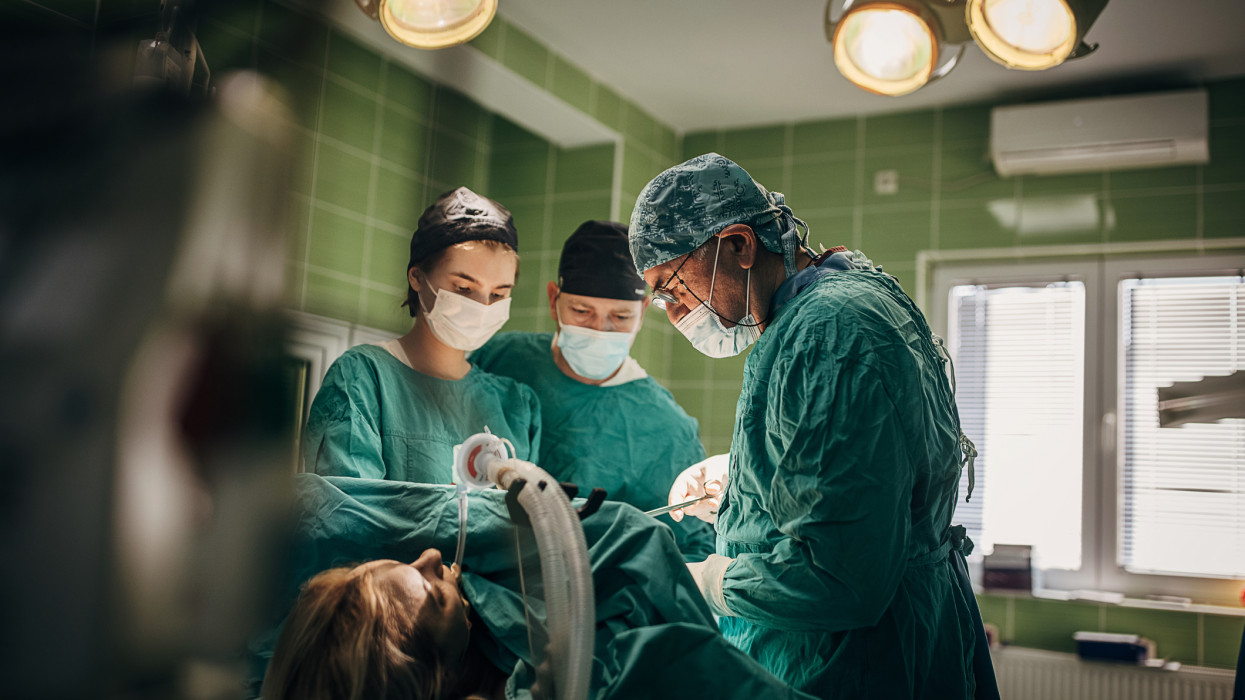 Group of surgeons performing surgery on a female patient in operating room.
