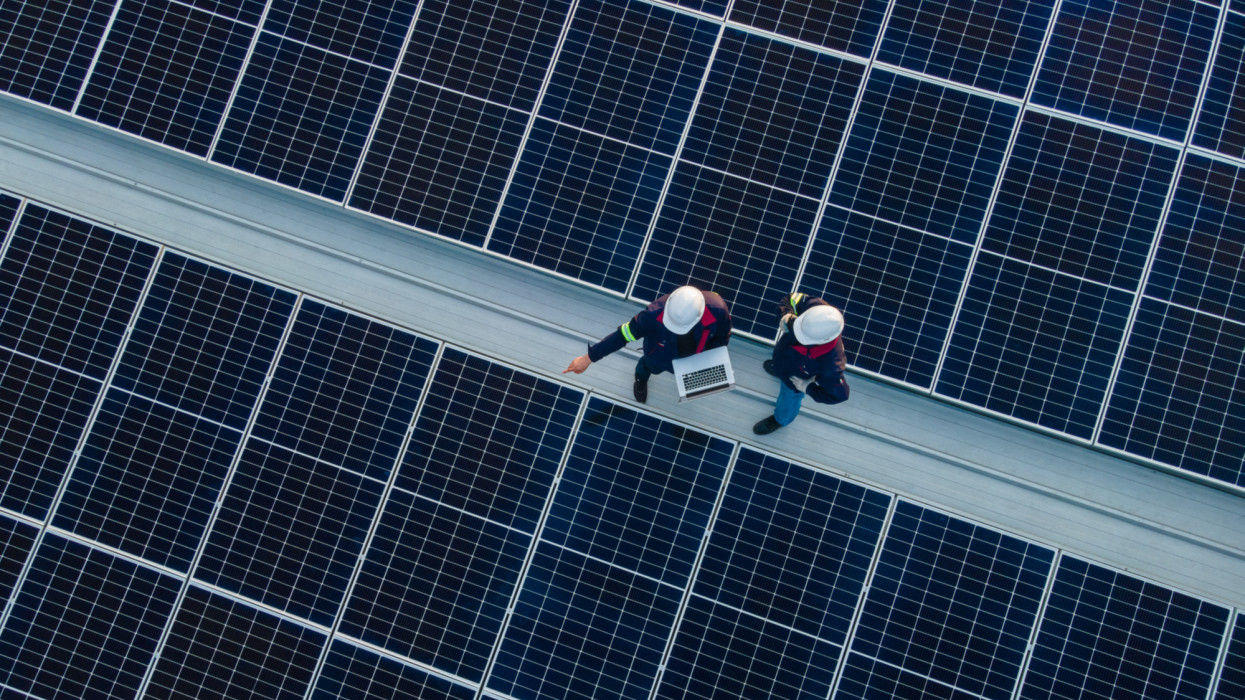 Aerial view of Engineer or Technician working on checking equipment in solar power plant on the roof of an industrial factory. Concept of installing solar cells on the roof.