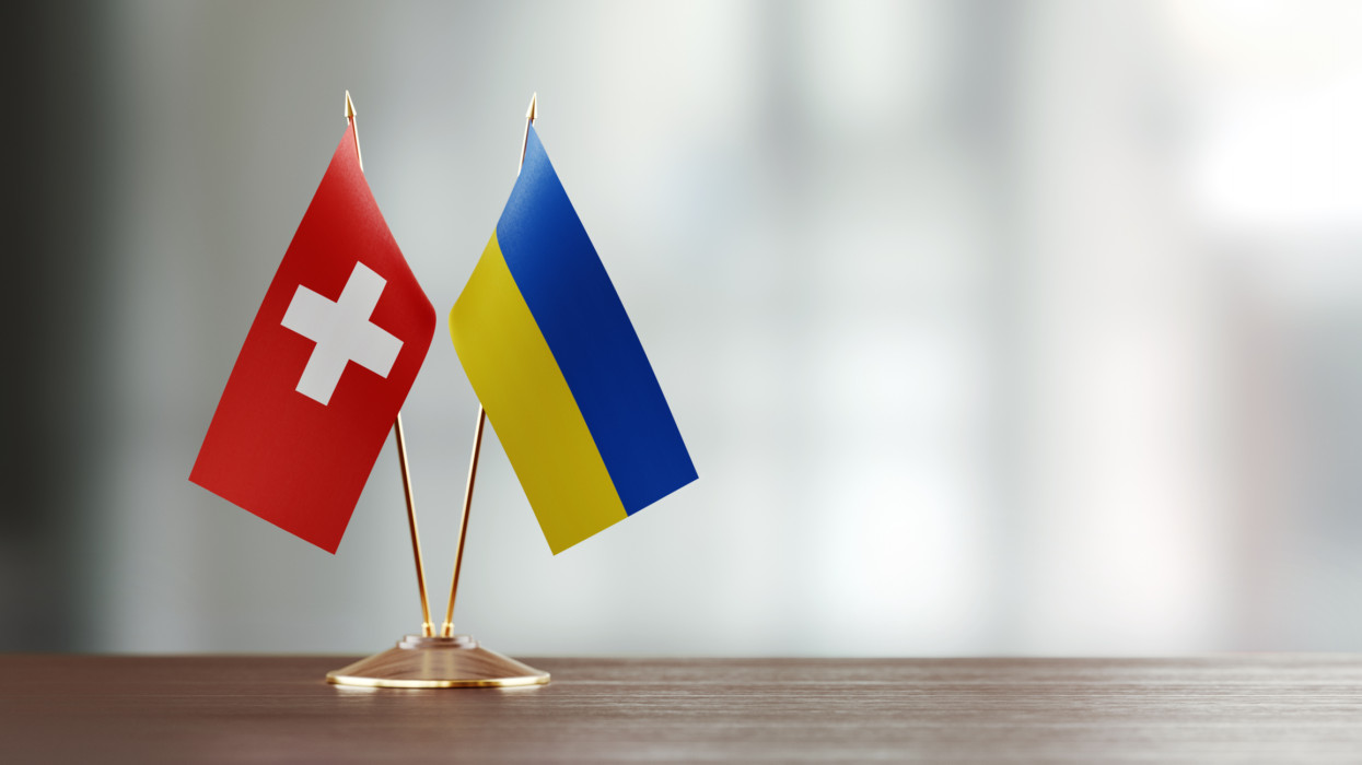 Swiss and Ukrainian flag pair on desk over defocused background. Horizontal composition with copy space and selective focus.