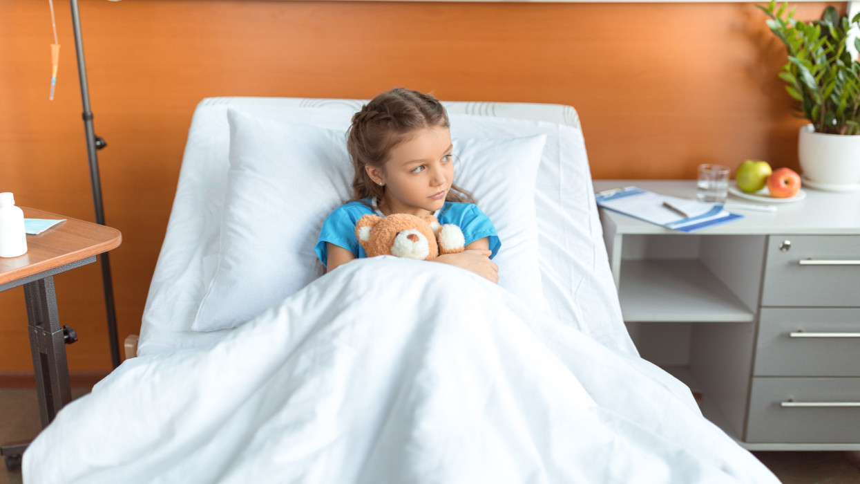 little adorable patient with teddy bear lying on bed in hospital