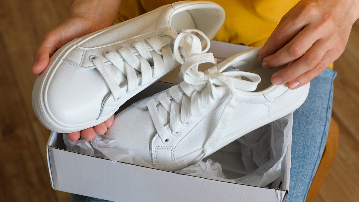 The girl takes out new clean white modern sneakers from the package. A woman or a teenager unpacks sports shoes from a box, at home or indoors. Ordering and Delivery of clothes and things at home. Stay at home. A fashionable and stylish lifestyle.