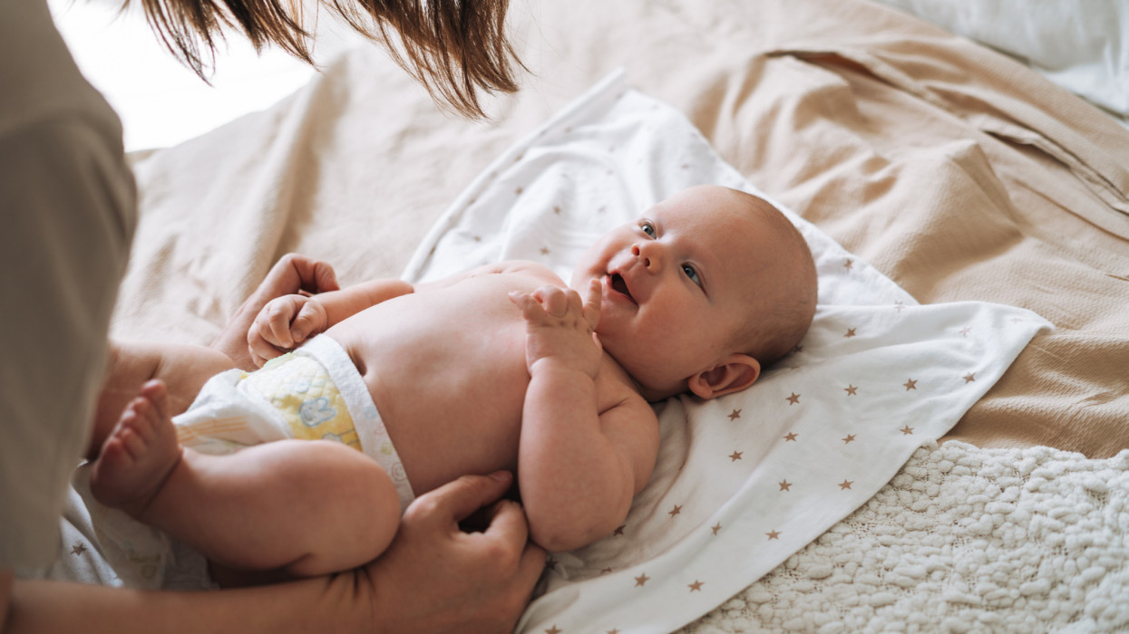 Felnőtt nő fiatal anya 2-3 hónapos kisfiúval fehér takarón fekve otthonában