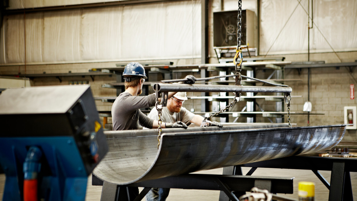 Steel workers adjusting position of brake press formed steel with crane