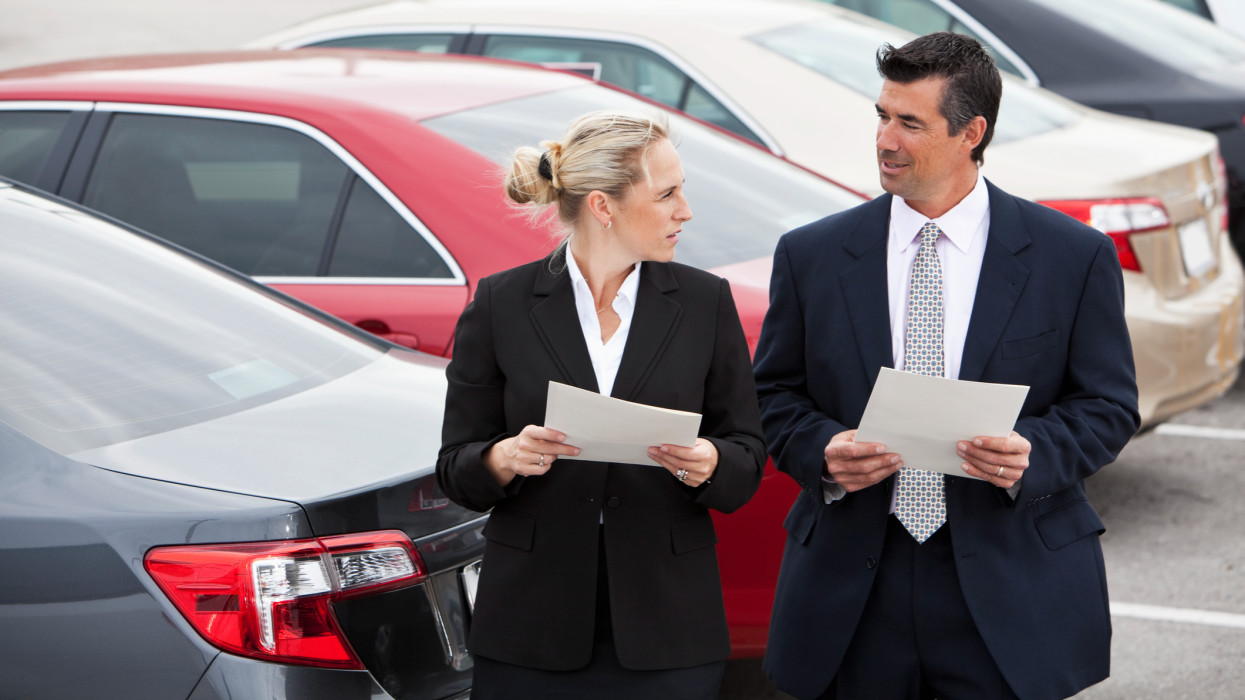 Businessman and businesswoman talking in parking lot.  Shallow DOF, focus on people in foreground.