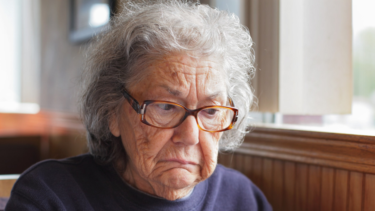 A sad-faced senior woman is sitting in a restaurant. Dont worry, she is not really this sad - she was just posing and making this face for the camera! :) Shallow depth of field.