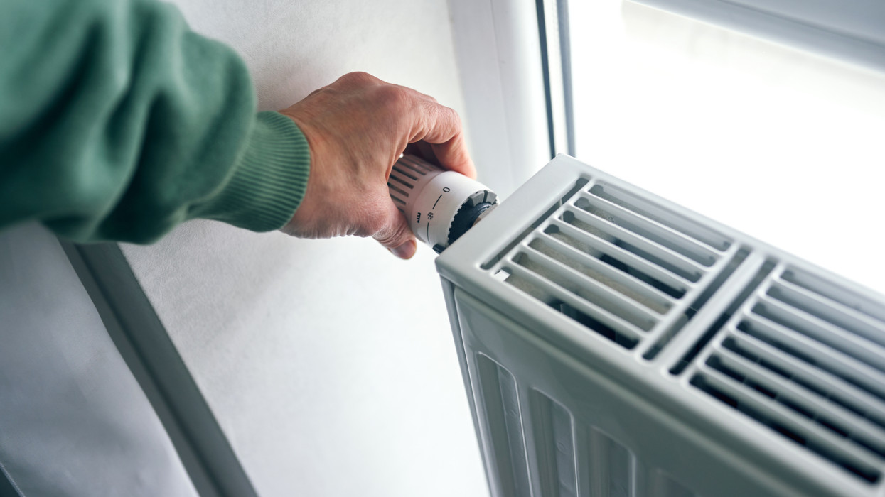 Közelkép a radiátor termosztátját szabályozó női kezekről. Egy nő növeli vagy csökkenti a hőmérsékletet a radiátoron a lakásban.