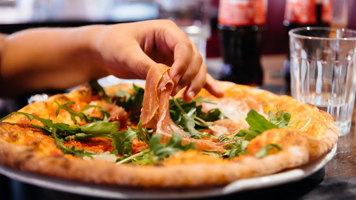 Hand of woman take ham pieces out from pizza plate in restaurant.