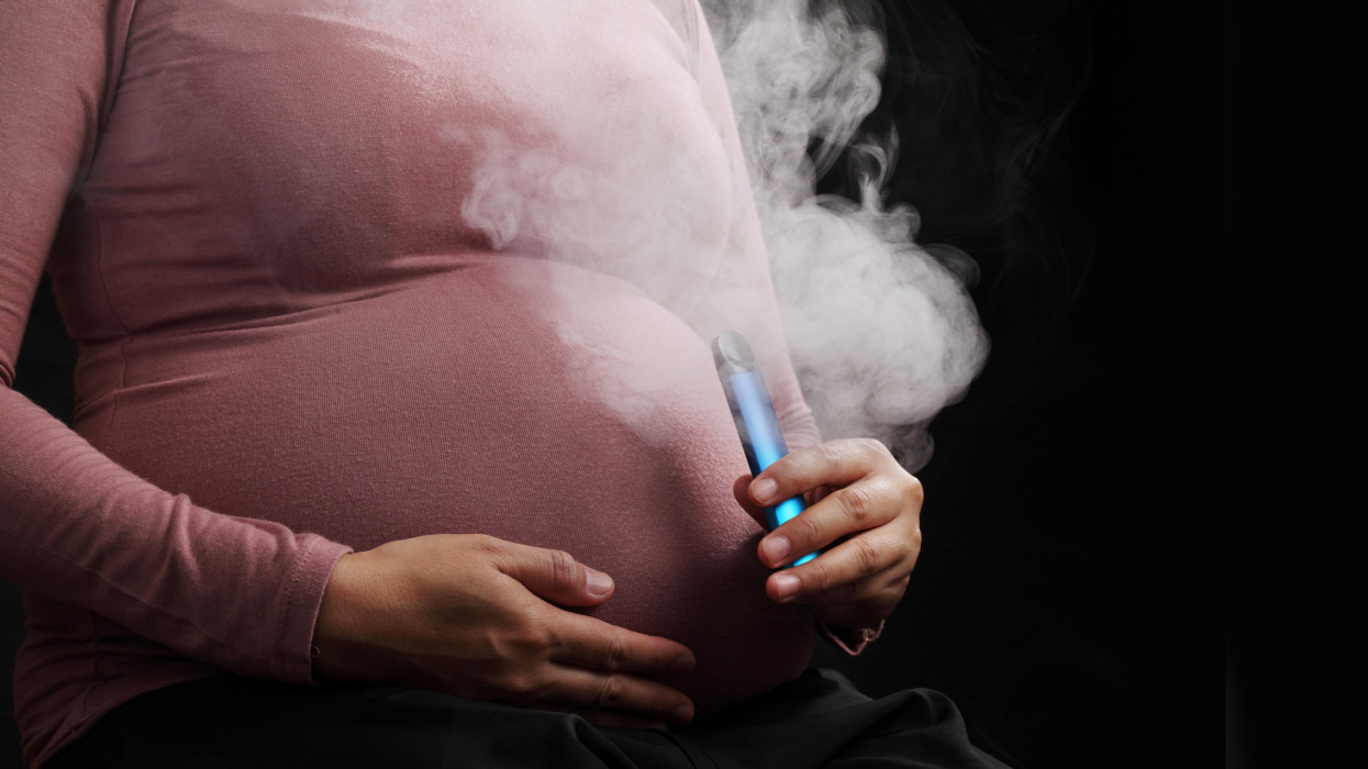Close up pregnant woman smoking e-cigarette isolated on black background