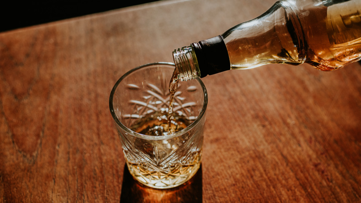 A bottle of whisky is poured into a cut glass tumbler over ice. Space for copy.