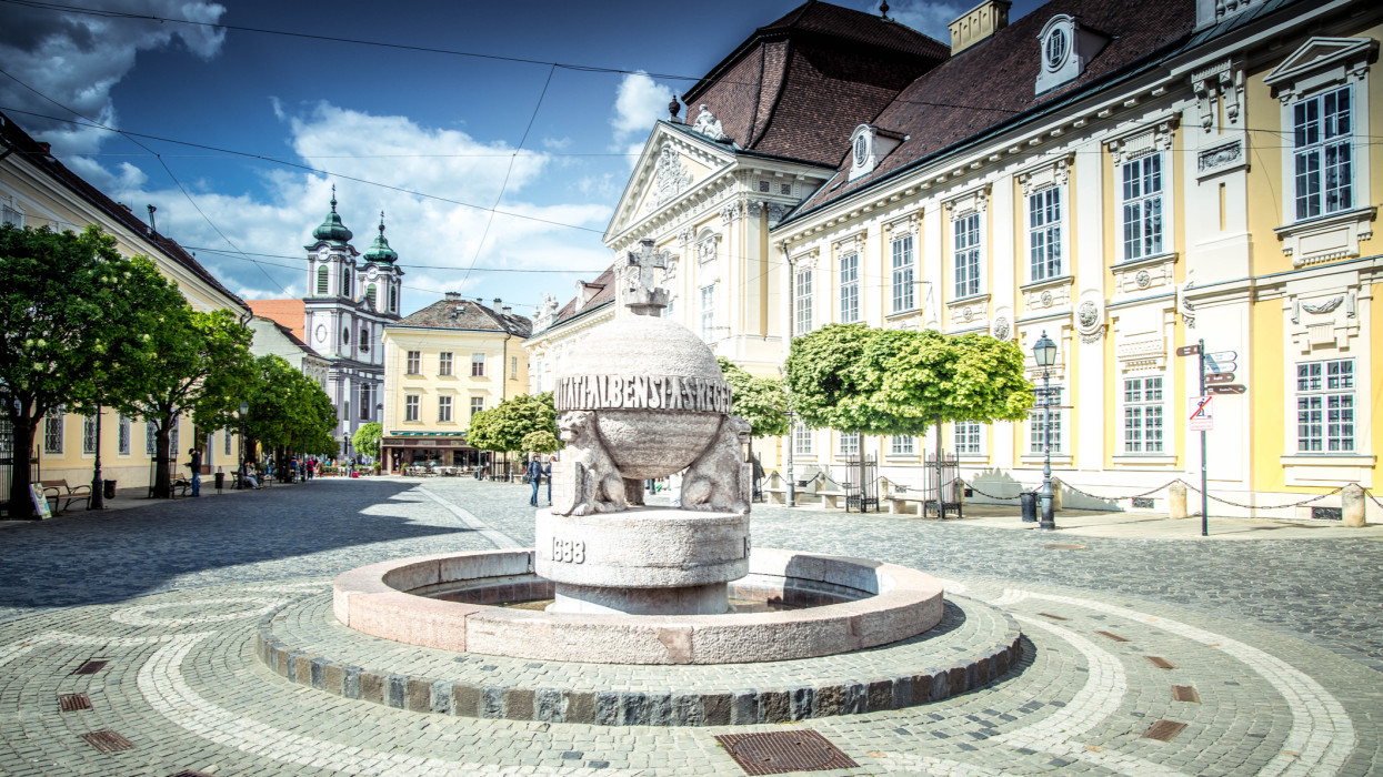 SzÃ©kesfehÃ©rvÃ¡r,  Hungary - April 26, 2023:  A fountain was built in the city square in the 1940s as a symbol of royal power in the form of an apple, topped with a cross and supported by lions. People enjoy the cold water in hot spring and summer days.