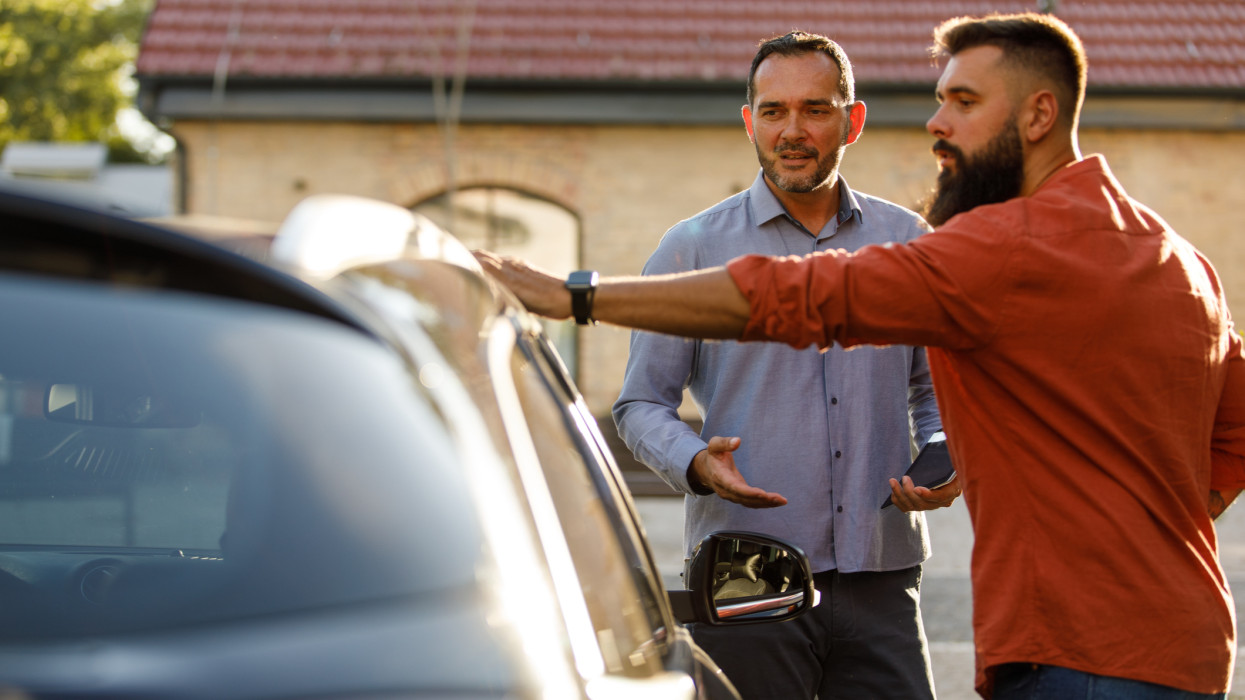 Copy space shot of mid adult salesman showing a car to a customer, sharing performances while inspecting the vehicle together.