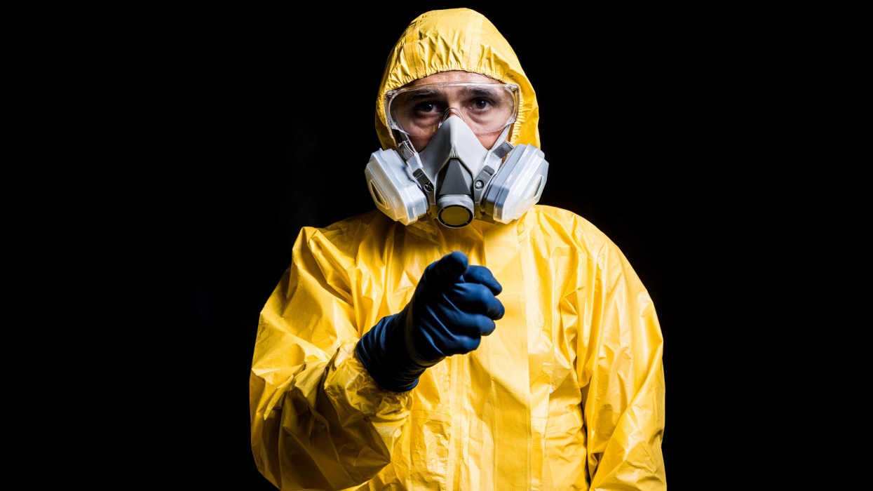 Portrait of technician wearing yellow nuclear protection suit, mask and goggles, pointing finger at camera. Concept of nuclear energy and pandemics.