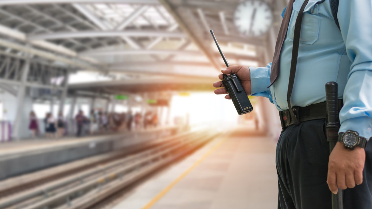 Professional security guard hand holding cb walkie-talkie radio in electric train station, copy space for text.