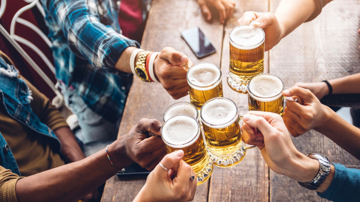 Emberek csoportja sörözik és koccintanak a sörözőben - Barátság koncepció, fiatalok szórakoznak együtt