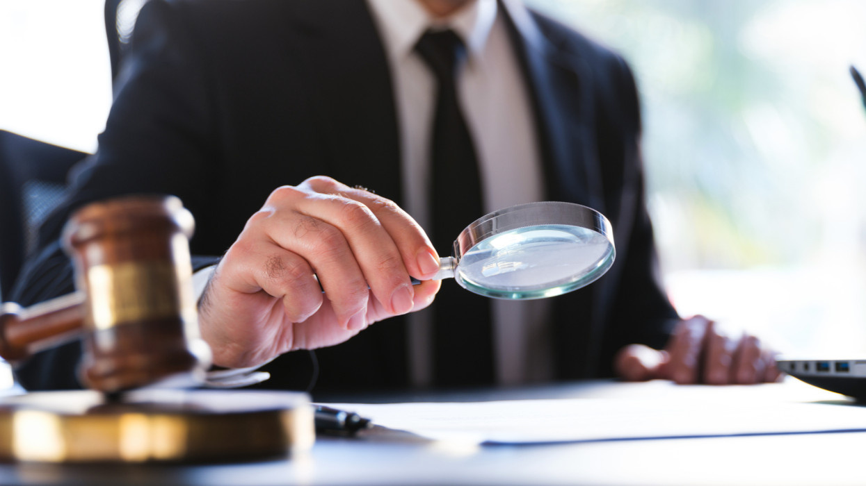 Man In Black Suit Reading A Legal Document Carefully Using Magnifying Glass