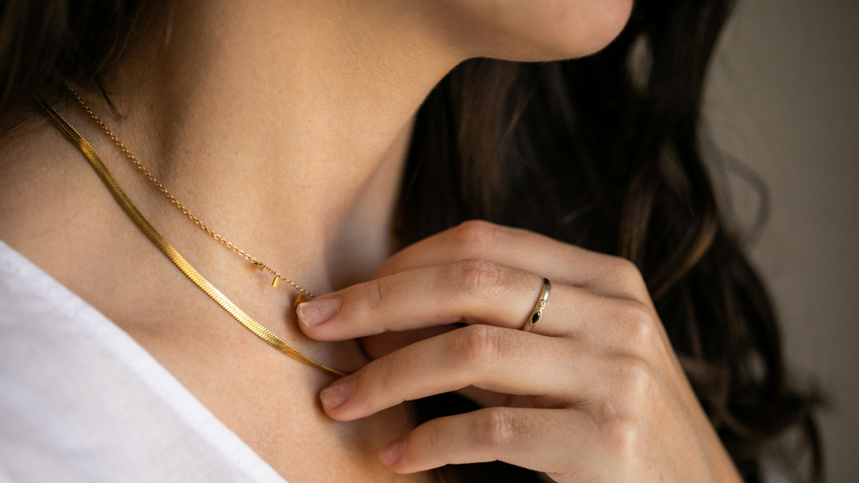 Close up of young woman wearing a gold ring touching her gold necklace