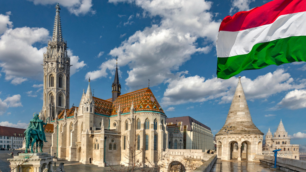 The Matthias Church with its roof decorated with colourful tiles with the equestrian statue of King Stephen I seen from The Fishermans Bastion and waving Hungarian flag in Budapest, Hungary
