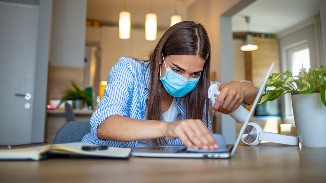 Woman in the office using disinfectant for sanitizing monitor surface during COVID-19 pandemic. Hygiene and virus prevention at work or at home. Coronavirus. Sanitizer. Woman working in quarantine.