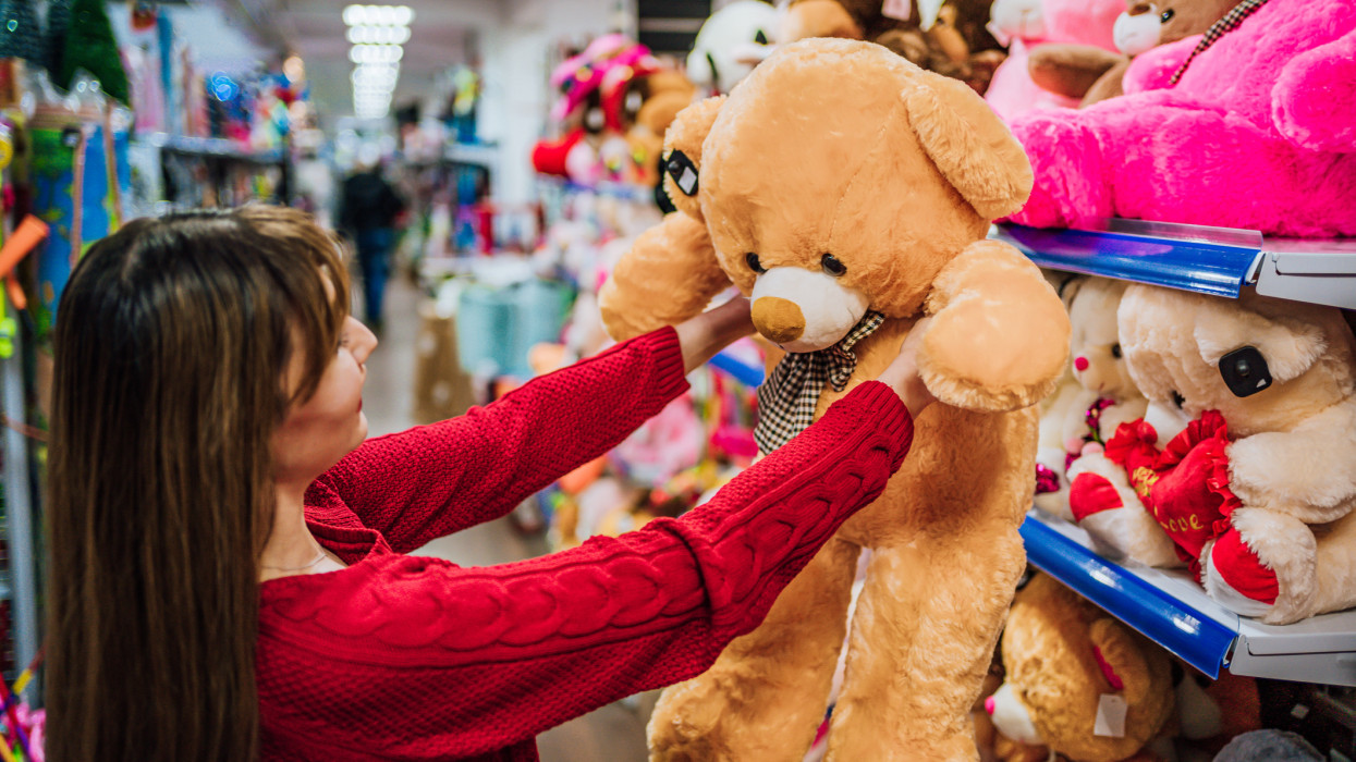 Young cheerful woman choosing teddy bear in a toy store