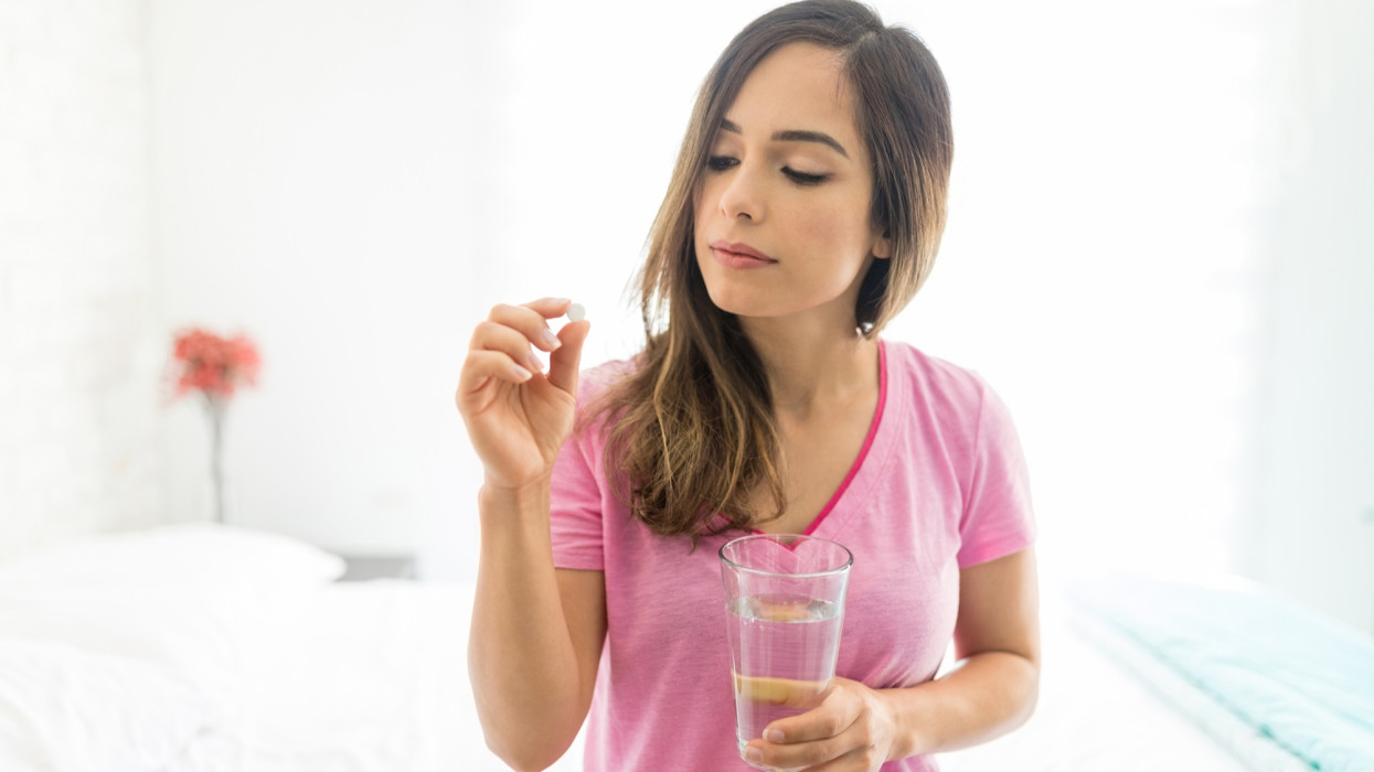 Sick mid adult woman taking dose of medicine while sitting on bed