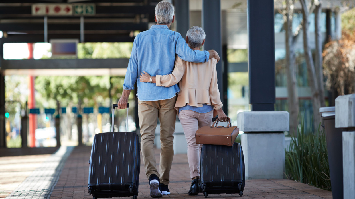 Senior couple walking together on public transport station, with rolling suitcases and bag