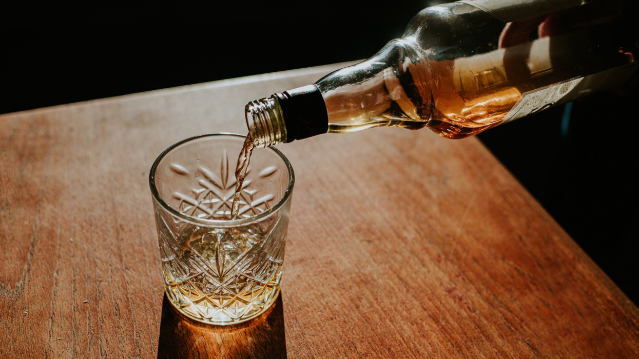 A bottle of whisky is poured into a cut glass tumbler over ice. Space for copy.