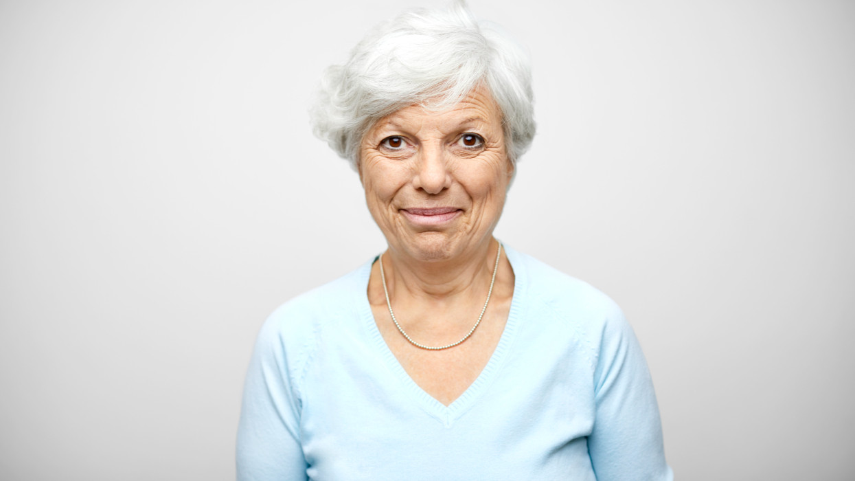 Portrait of Hispanic senior woman. Elderly female is against gray background. She is wearing casual.
