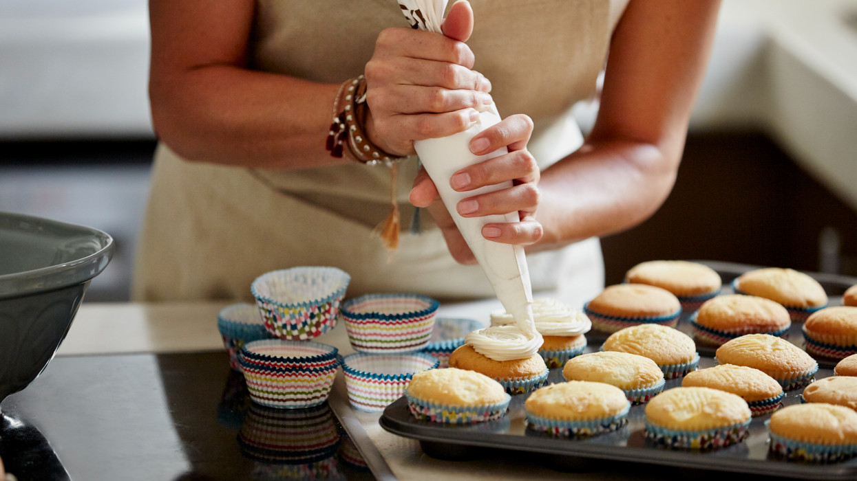 Midsection of woman icing cupcakes at kitchen counter