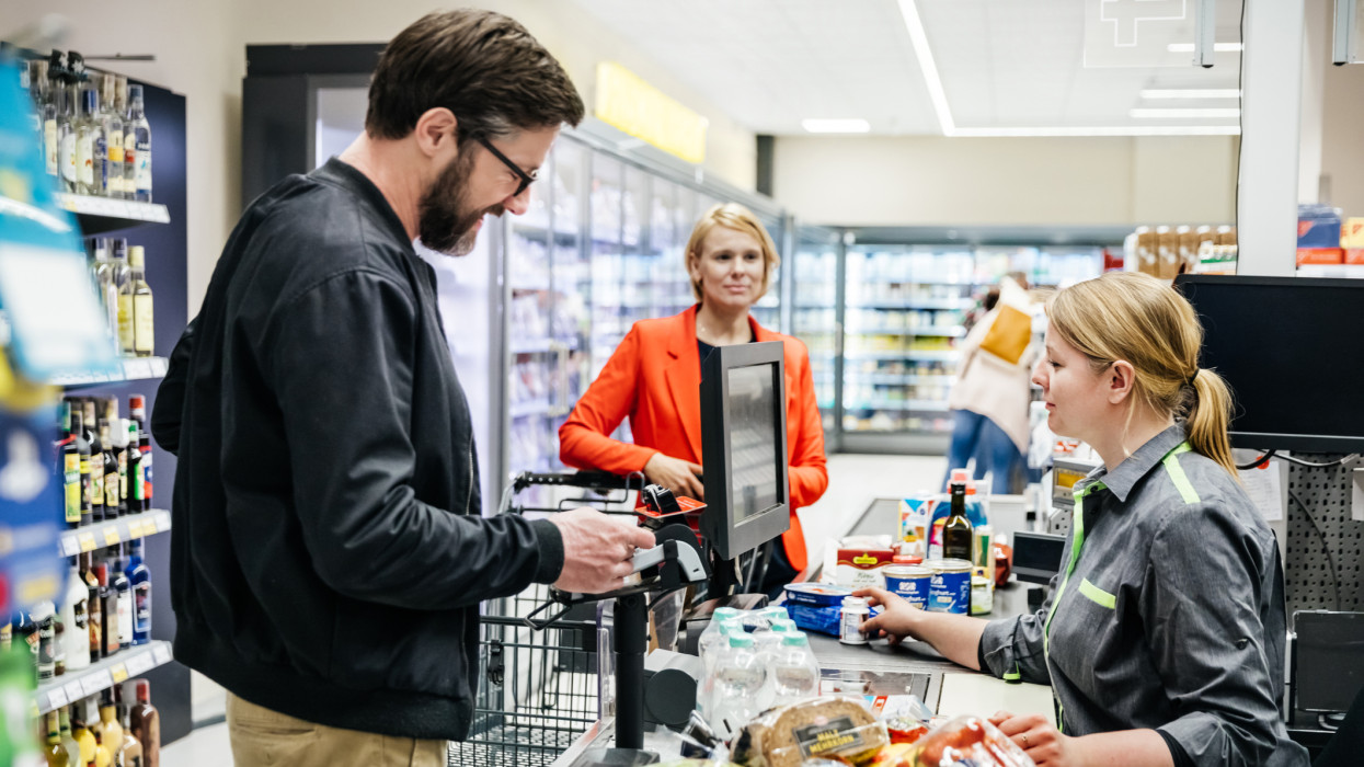 A mature man and his wife paying for their groceries at the checkout in their local supermarket.