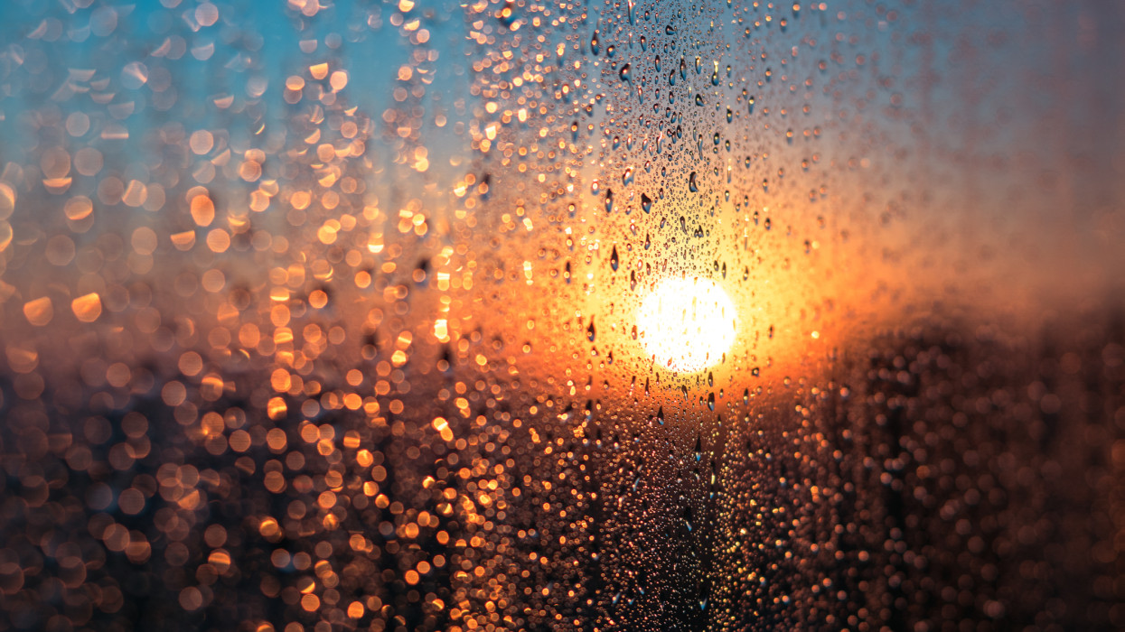 Wet Window with Condensation Water Against Sunrise or Sunset Glow in Cold Winter Day, Warm Indoor