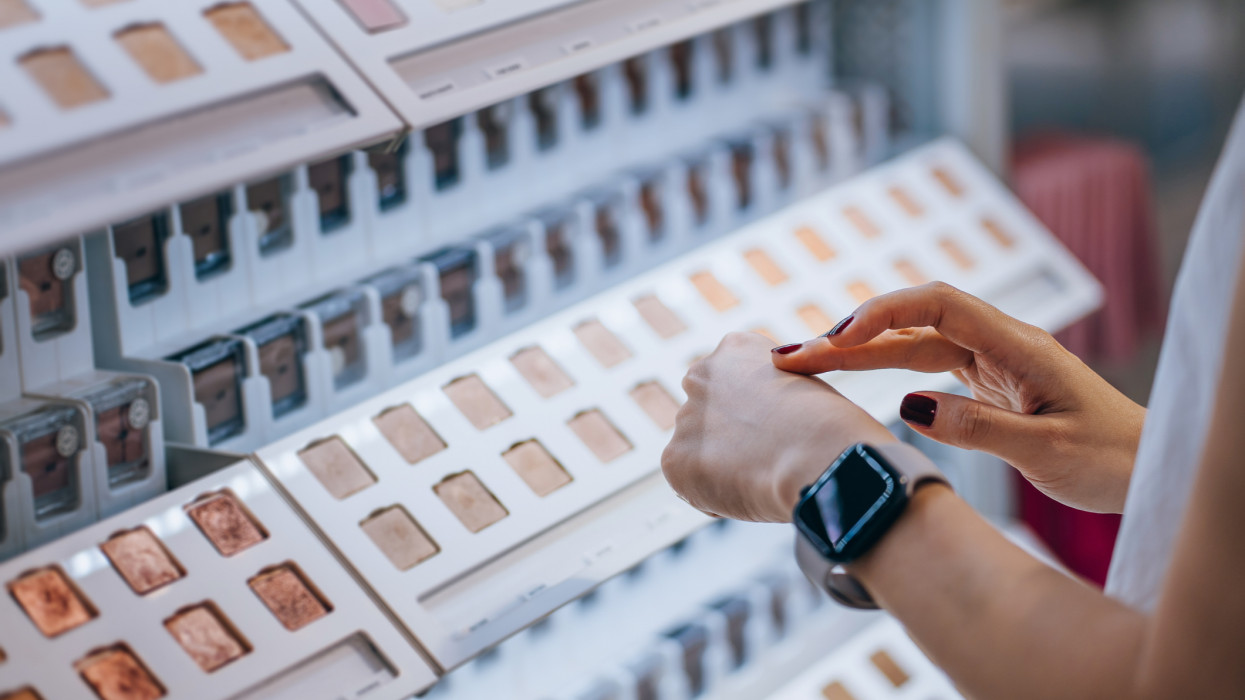 Close up of a young woman shopping in a beauty store, applying eye shadow tester on her hand. Cosmetics, make-up, beauty products shopping concept