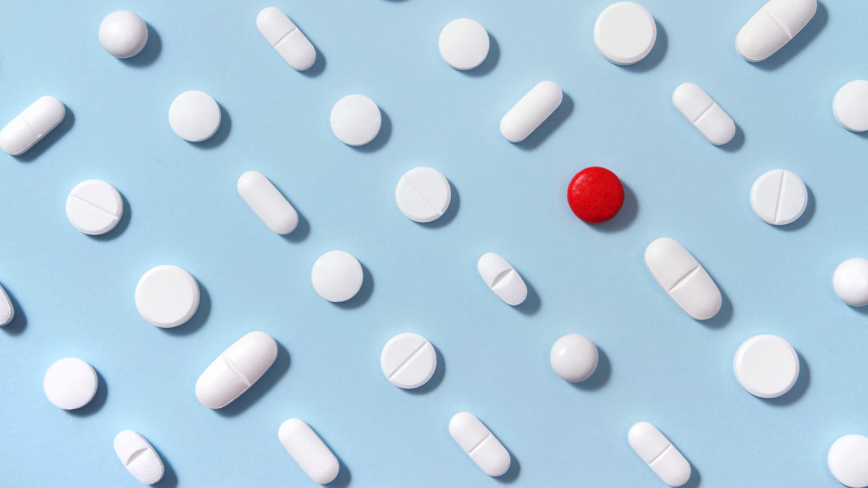 White pills arrangement on soft blue background with one red pill standing out from them
