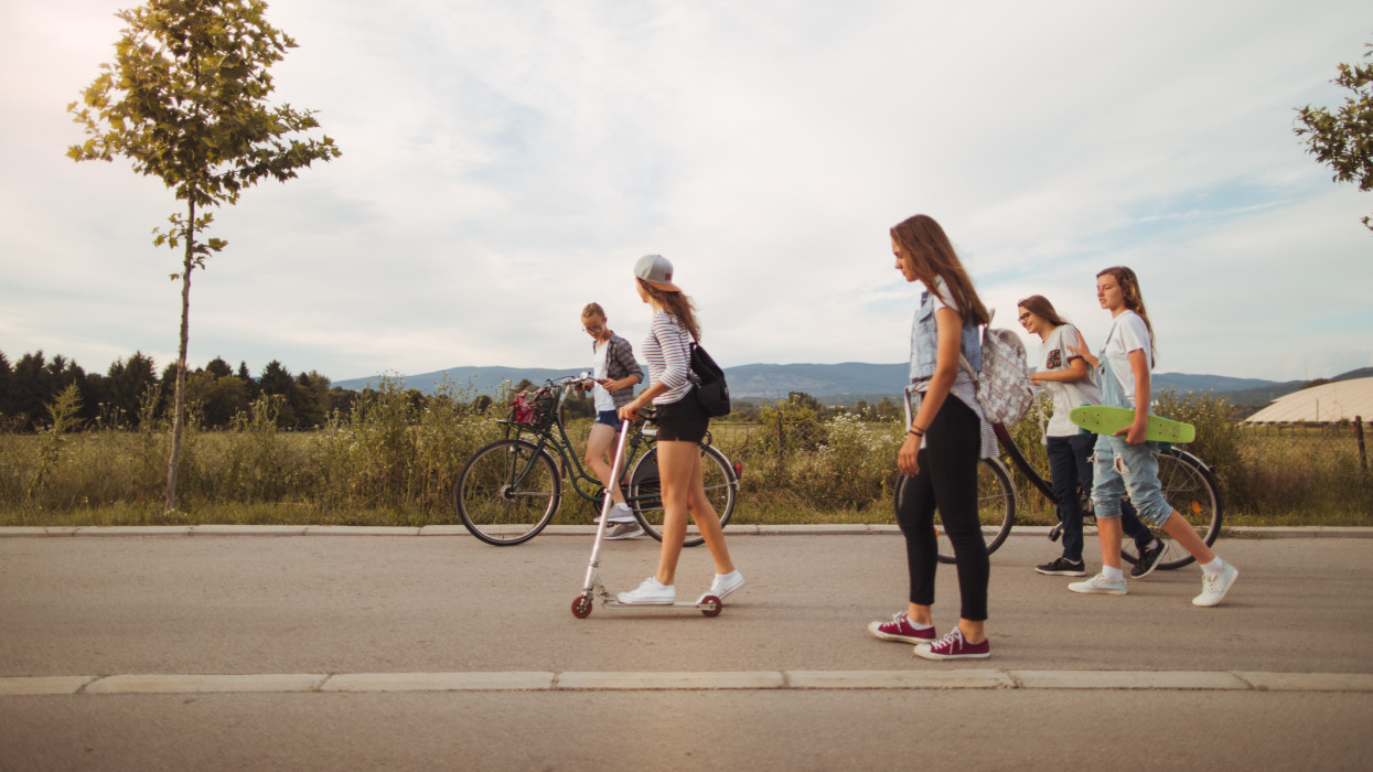Photo of a teenage girls spending free afternoon together, riding bicycles, push scooters and skateboards