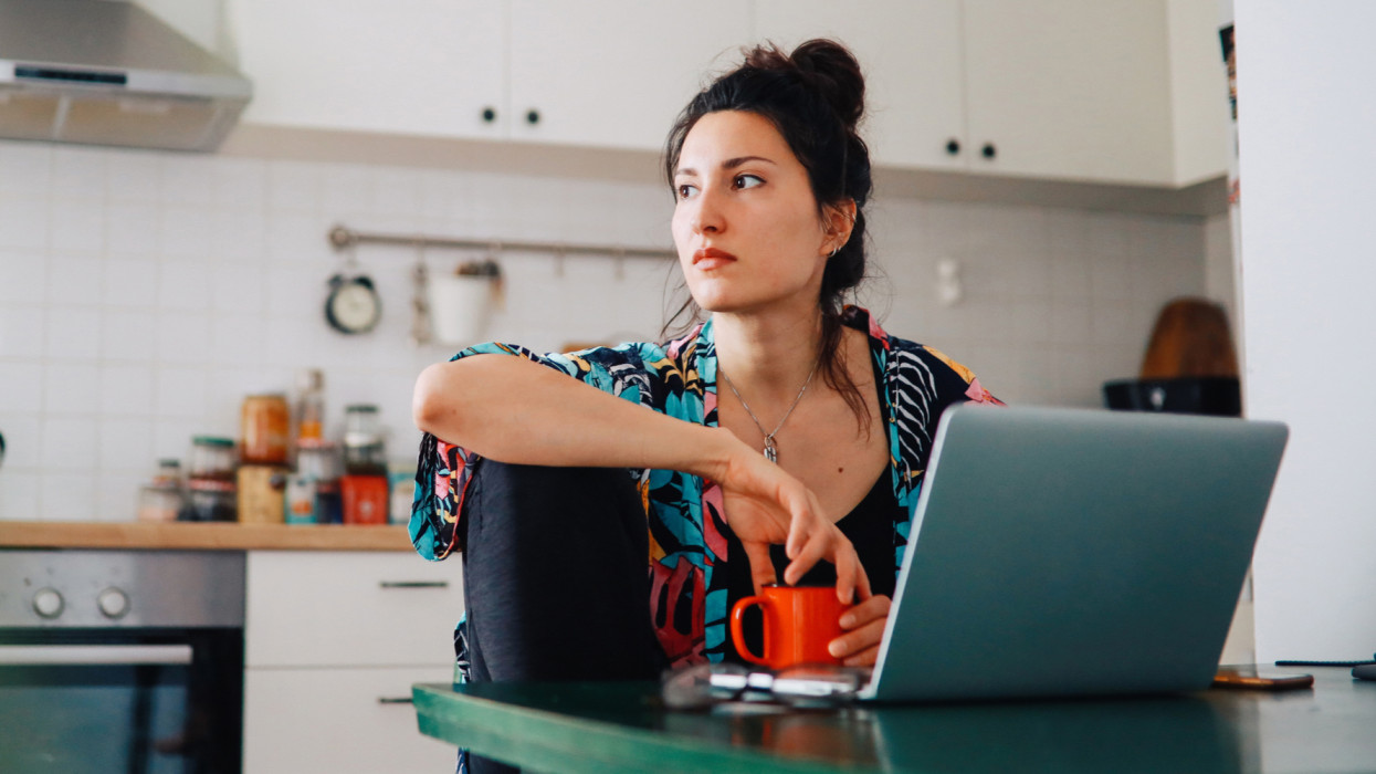 Young woman sitting in her kitchen while finishing work on the laptop, as she is instructed to work from home during the coronavirus social distancing.