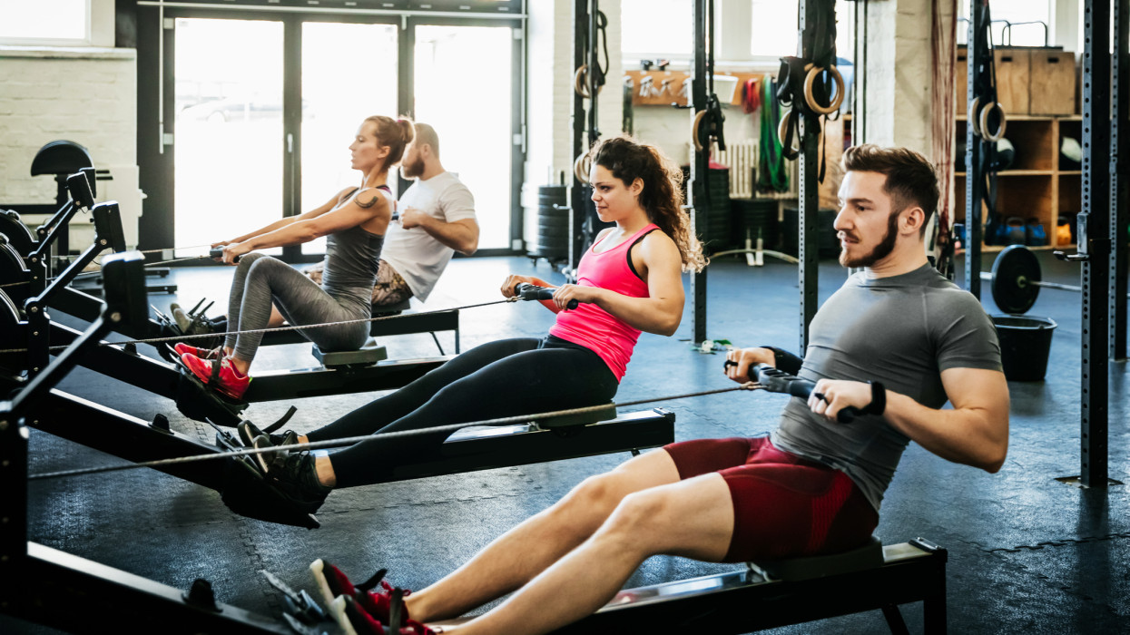 A group of fitness enthusiasts working out together at the gym using rowing machines.