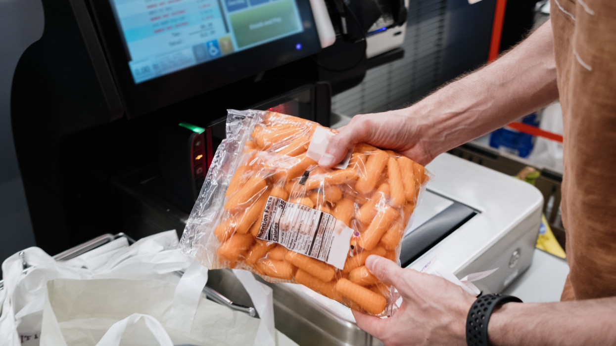 Close-up of unrecognizable white man purchasing groceries at self-checkout kiosk in supermarket