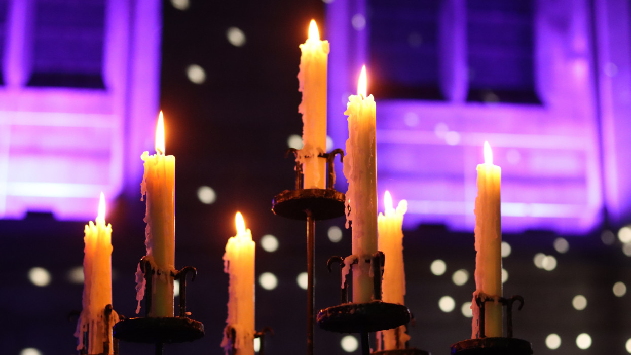 Candles burning in a traditional metal candlestick holder, inside a church at night