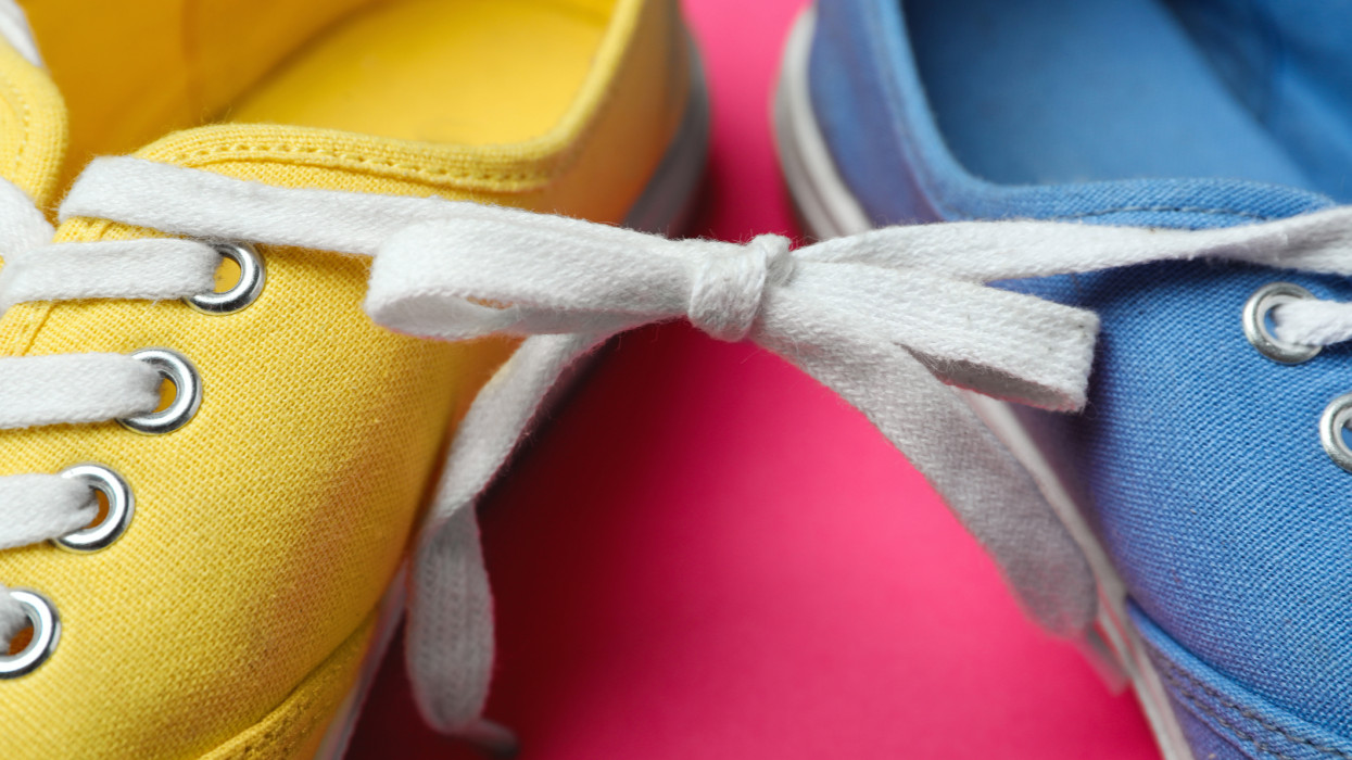 Shoes tied together on pink background, closeup. April Fools Day