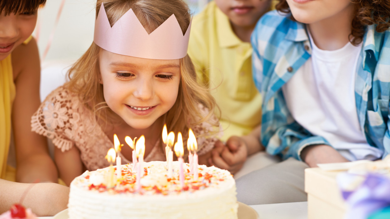 Lovely little girl and her friends looking at burning birthday candles